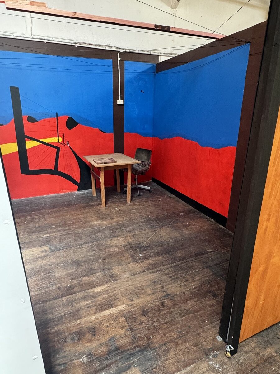 Ministry Building 4 Empty artist studio with a hand-painted red and blue mural, a small table and a chair
